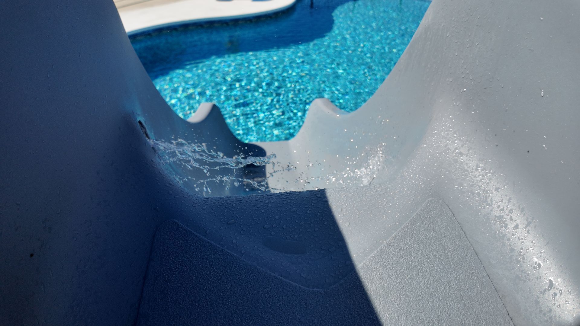 Blue plastic slide ending in a splash of water with a pool visible beyond it