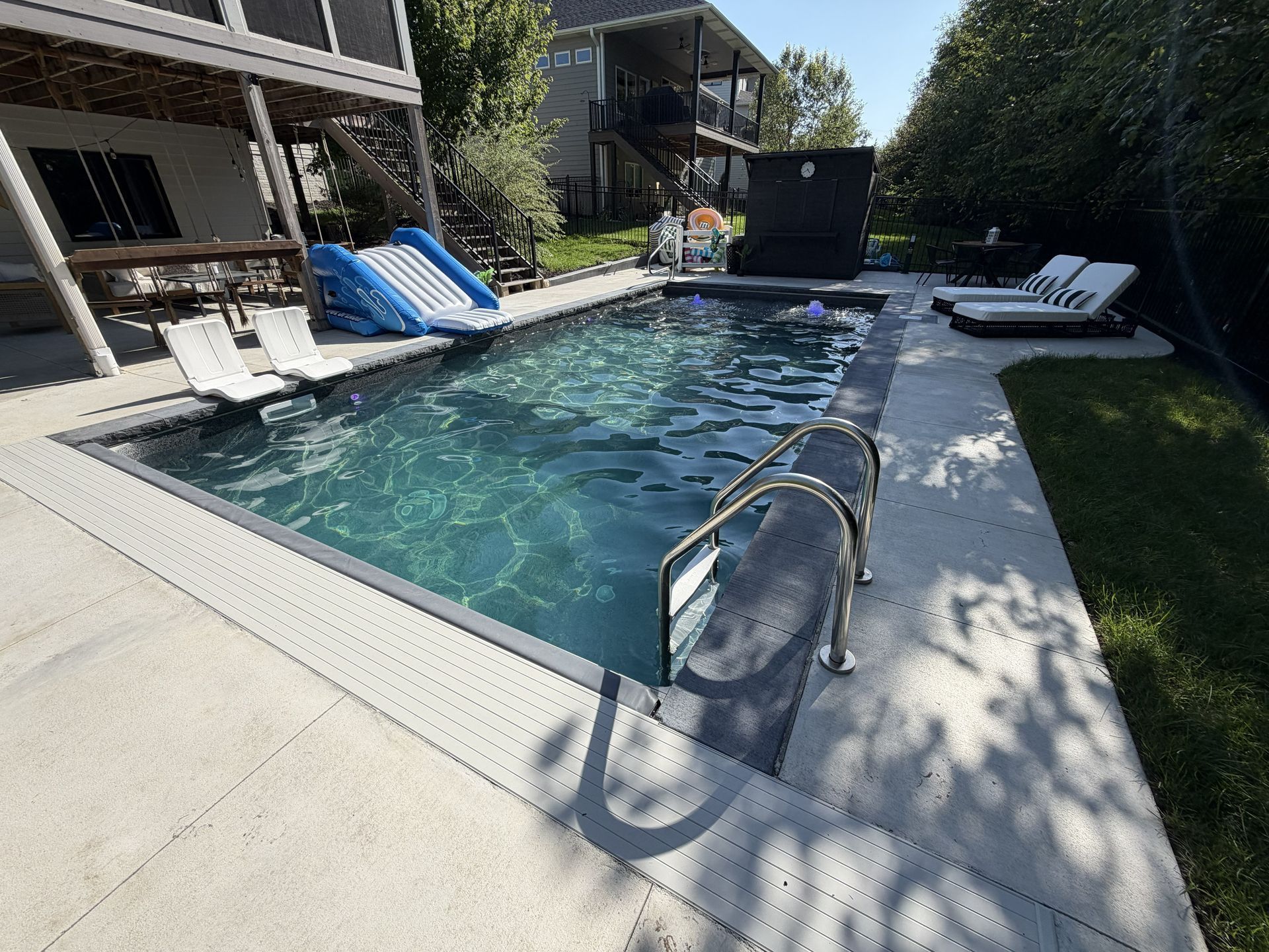 Backyard swimming pool with metal ladder, lounge chairs, and a sunny patio area