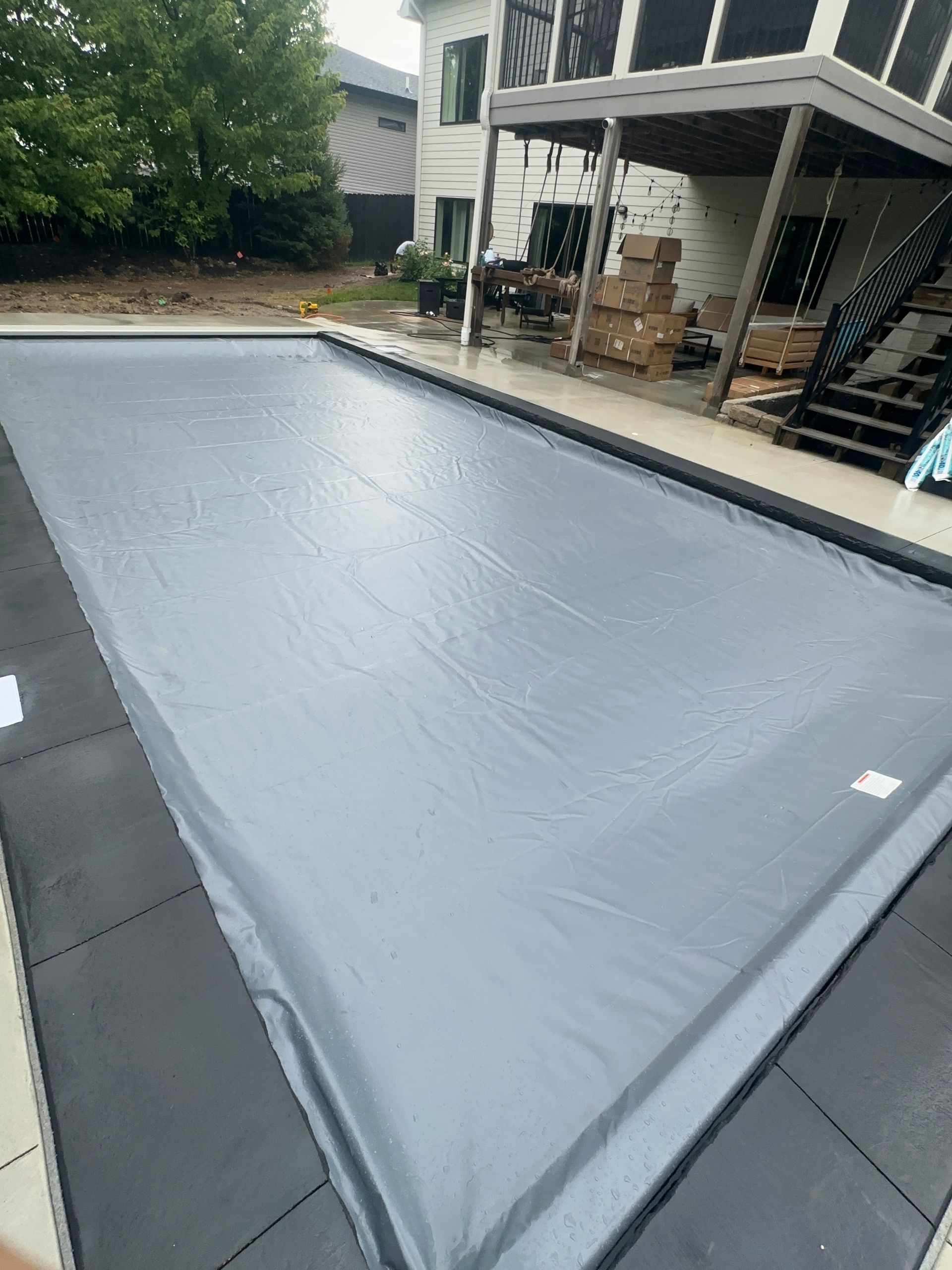 Covered swimming pool with a gray tarp in a backyard patio area