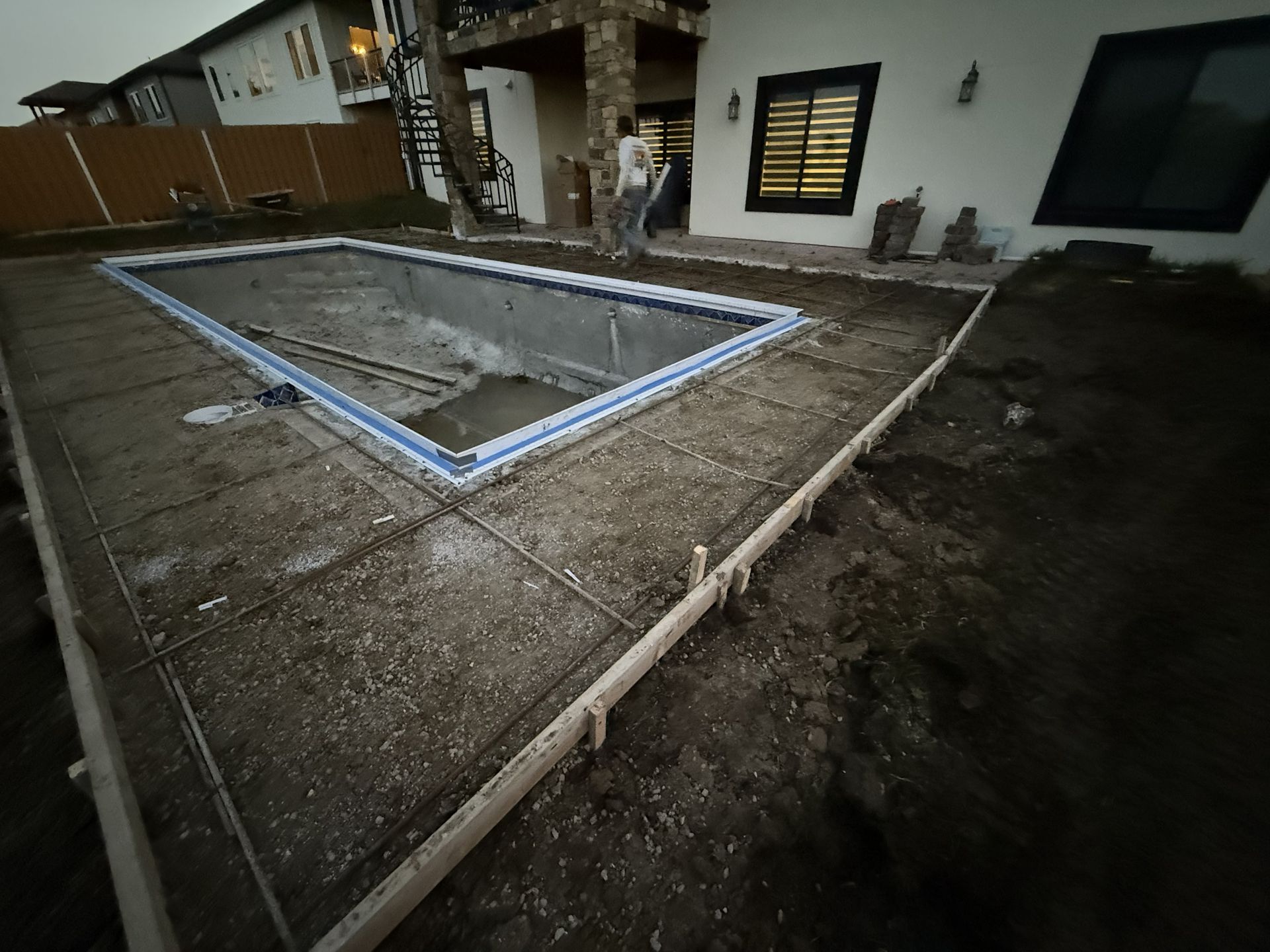 Partially built concrete patio with white border in front of a house at dusk