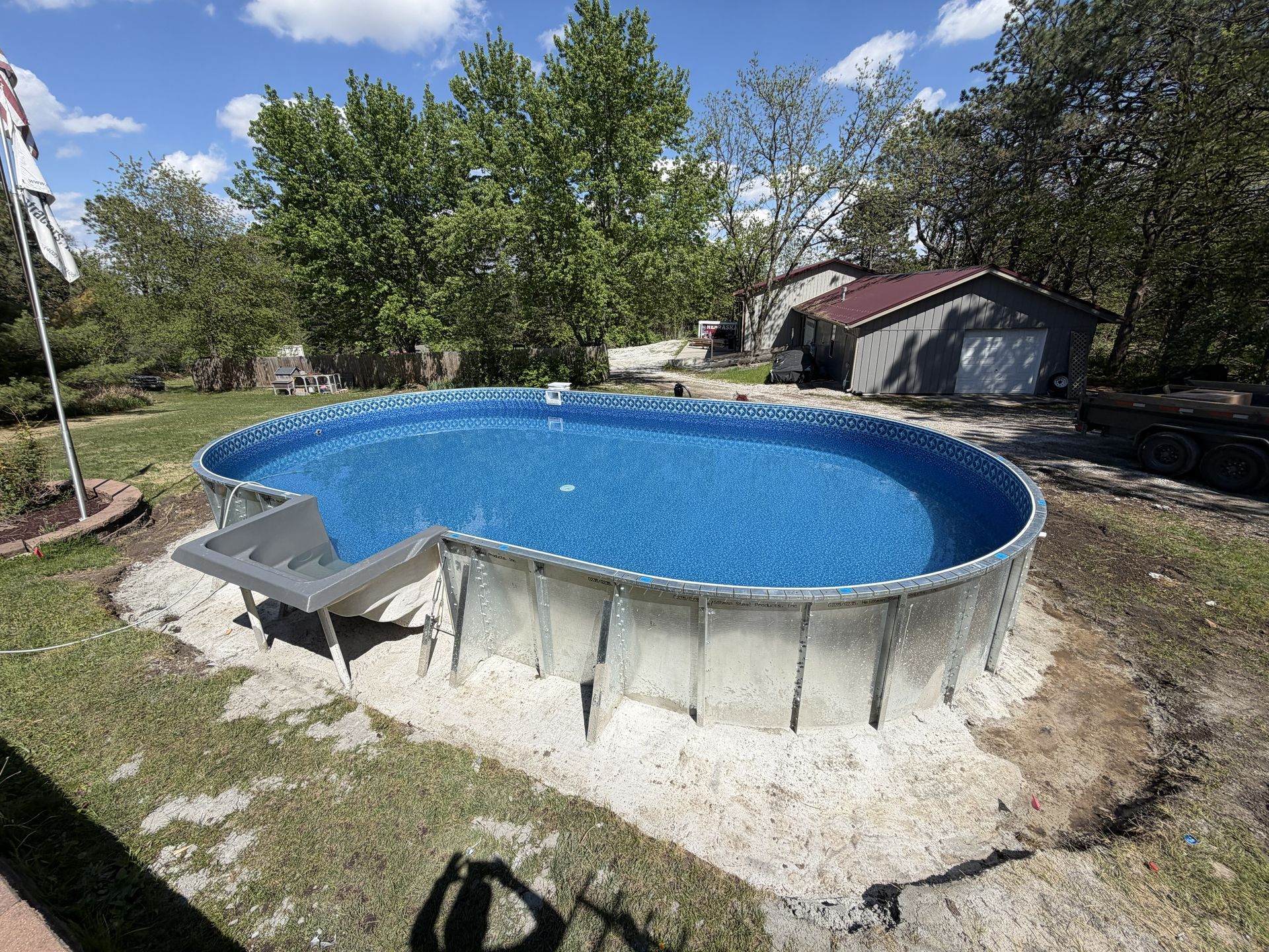 Above-ground backyard pool with blue water beside a small shed and trees on a sunny day