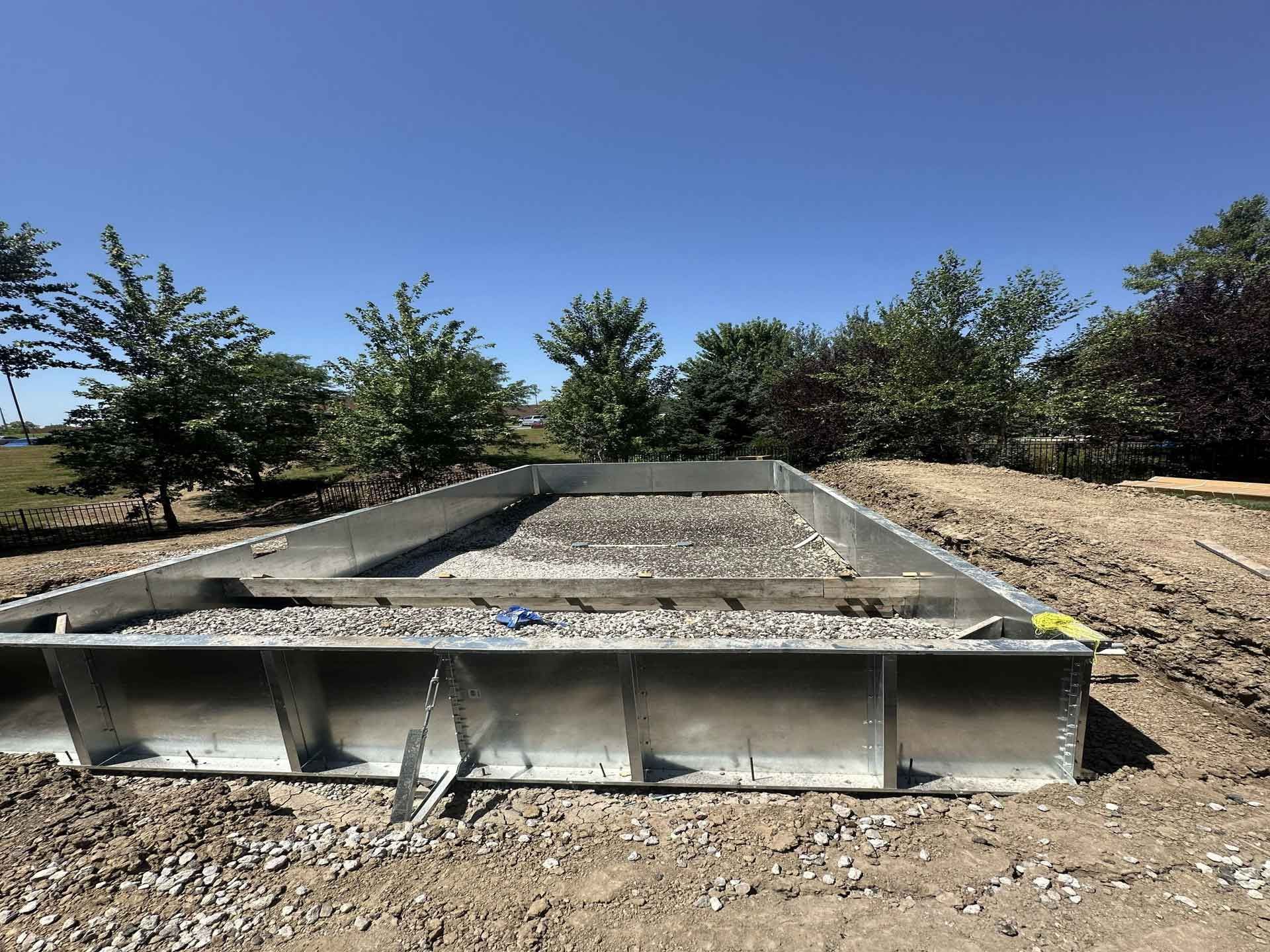Concrete stormwater basin with gravel and sloped sides in a sunny outdoor lot.