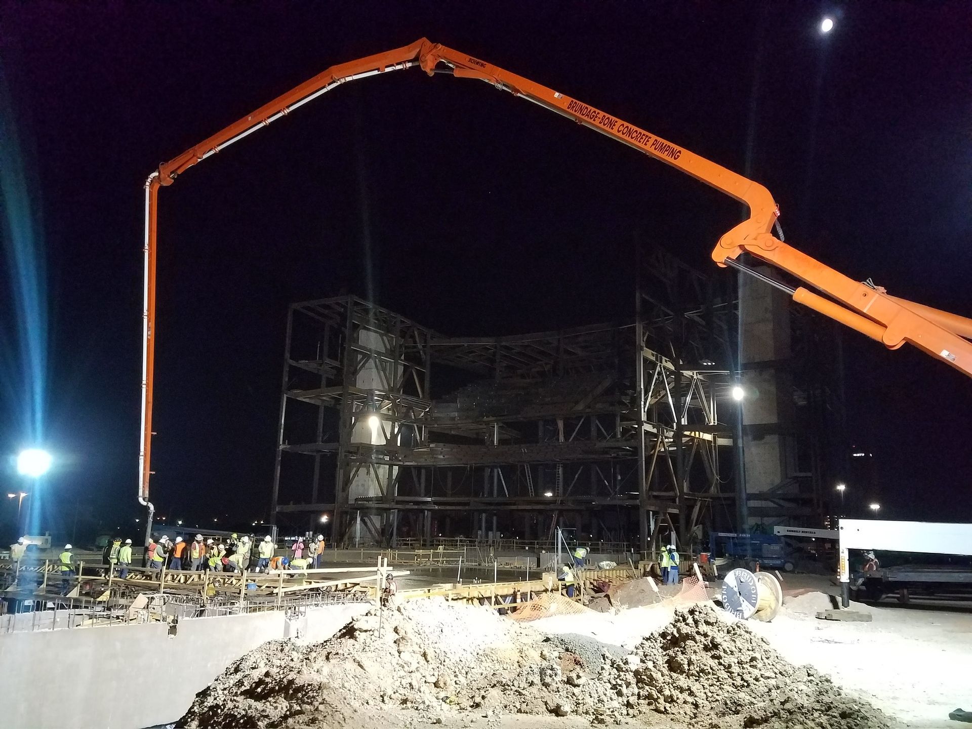 A construction site at night with a concrete pump in the foreground