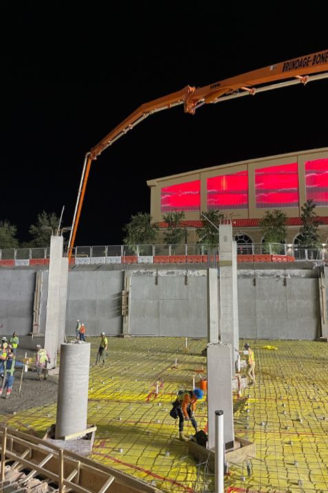 A concrete pump is being used to pour concrete on a construction site at night.