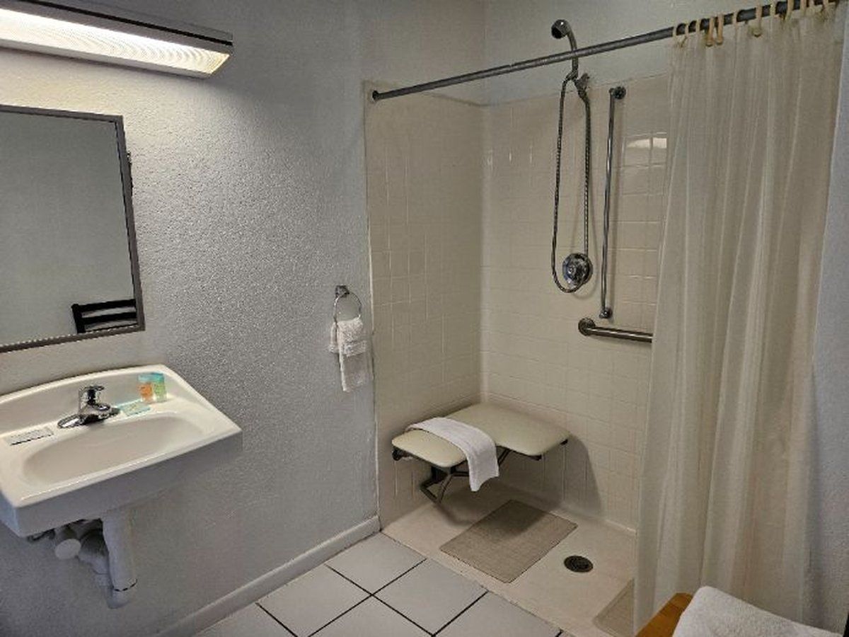 Bathroom with a low-entry shower, grab bar, folding seat, and pedestal sink
