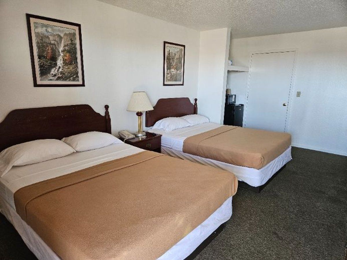 Hotel room with two double beds, framed art, lamp, and door