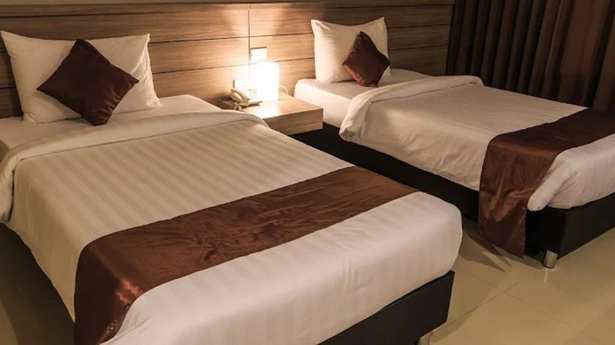 Two beds in a hotel room with white linens, brown accents, and a nightstand with lamp