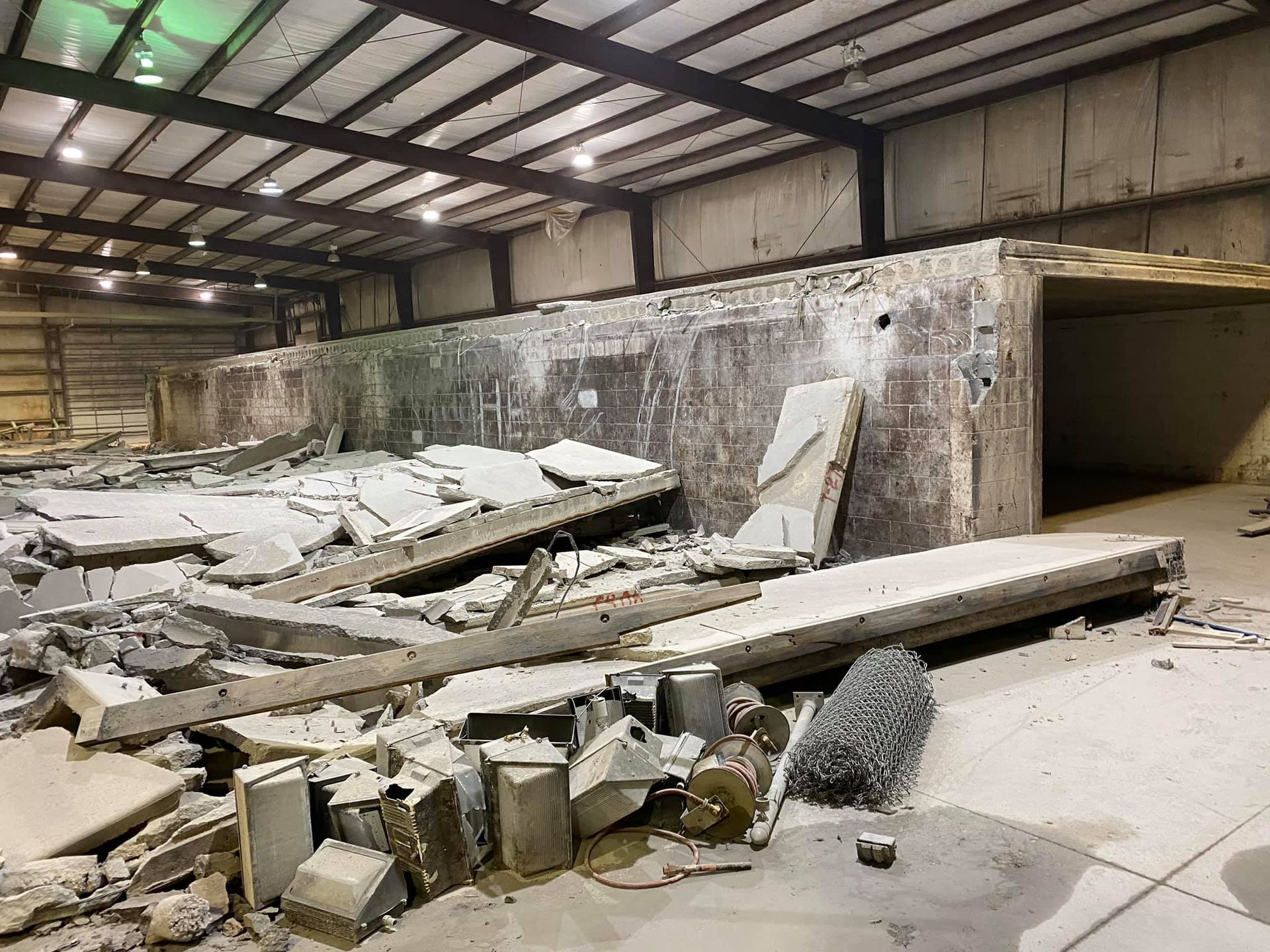 Collapsed industrial warehouse interior with rubble, broken concrete slabs, and debris scattered across the floor
