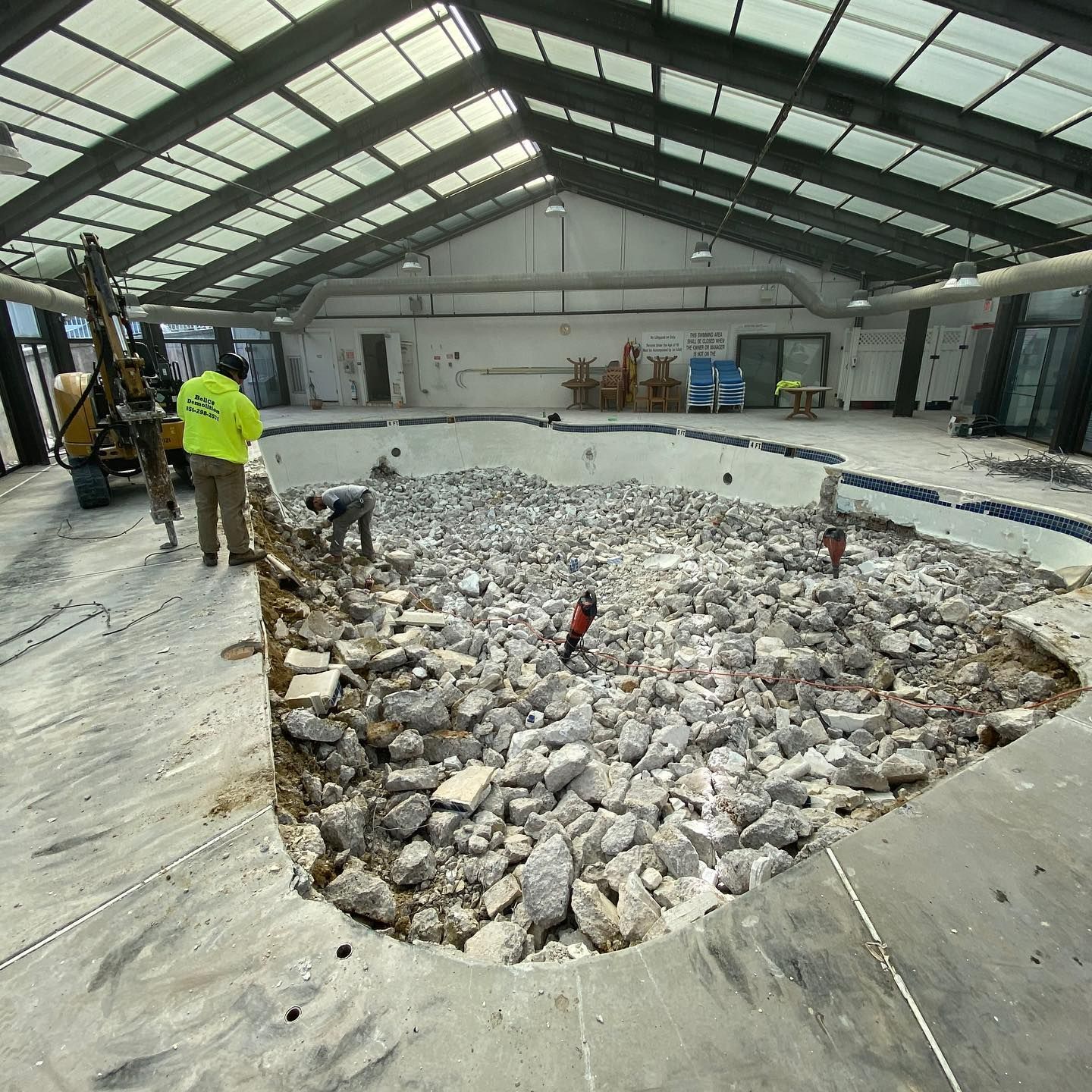 Construction crew breaking up a concrete floor inside a large industrial warehouse.