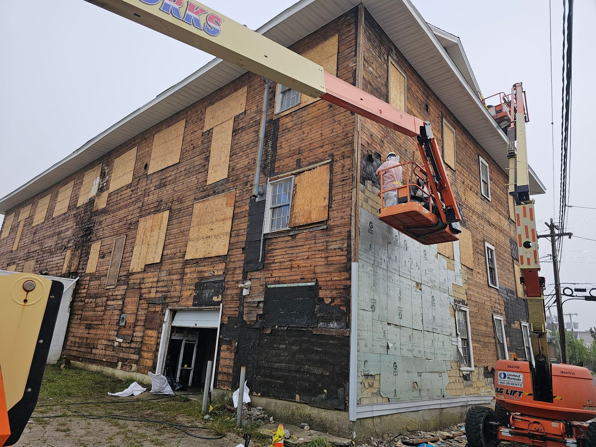 Workers in orange lifts repair the exterior wall of a brick building.