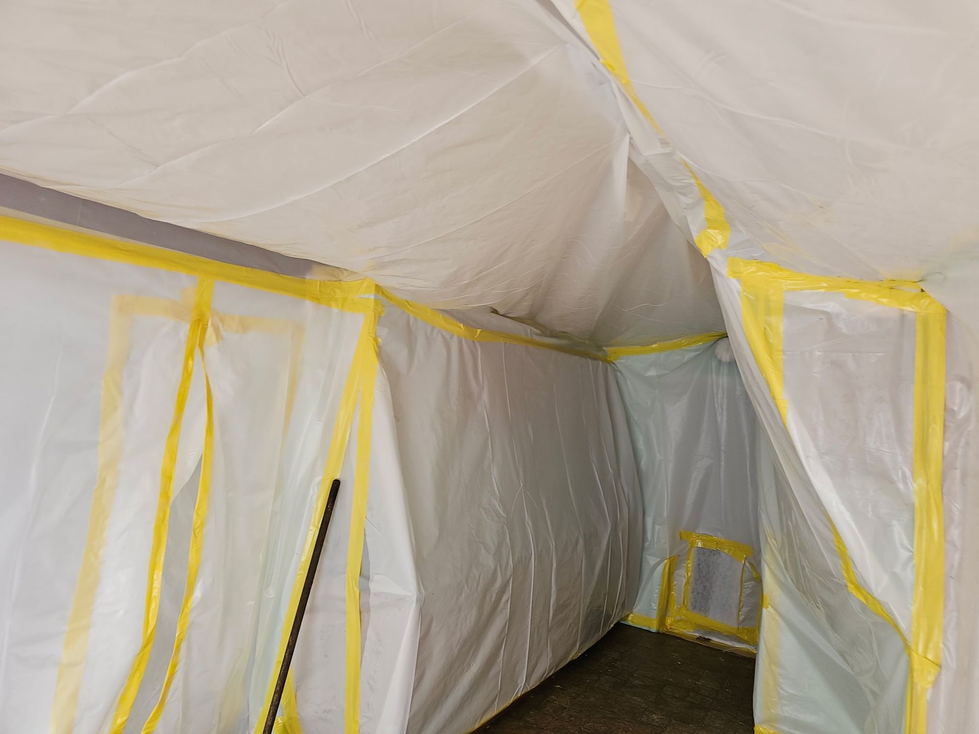 Plastic-covered room with yellow tape, resembling a sealed construction or cleanup area