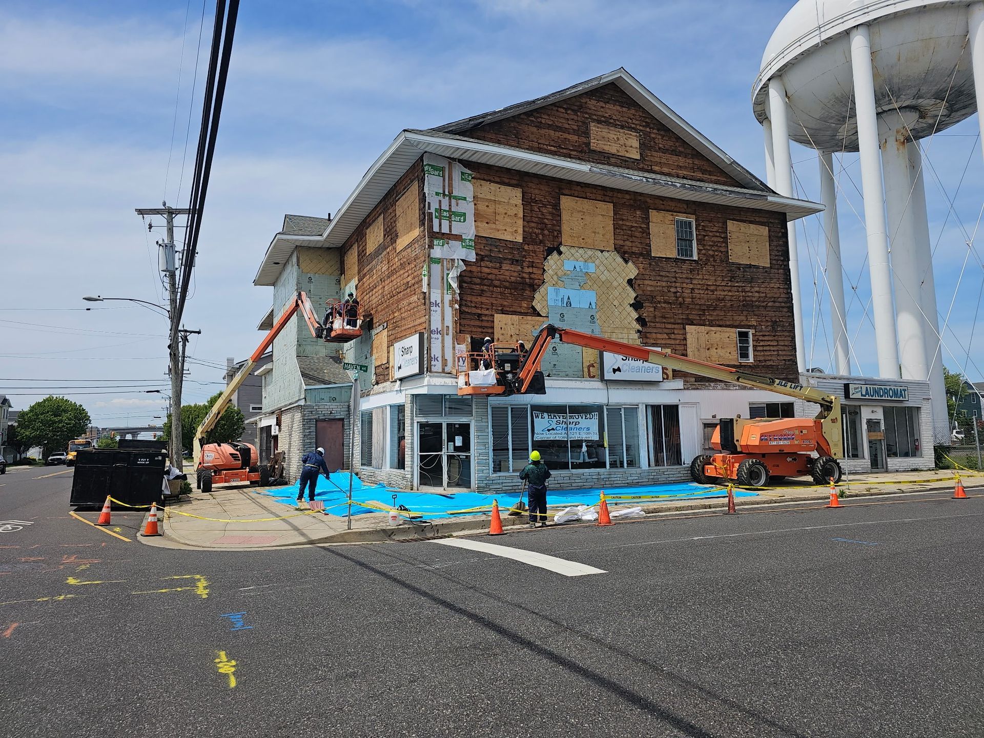 Street corner with a brick building under construction, painted mural, orange van, and a water tower nearby.