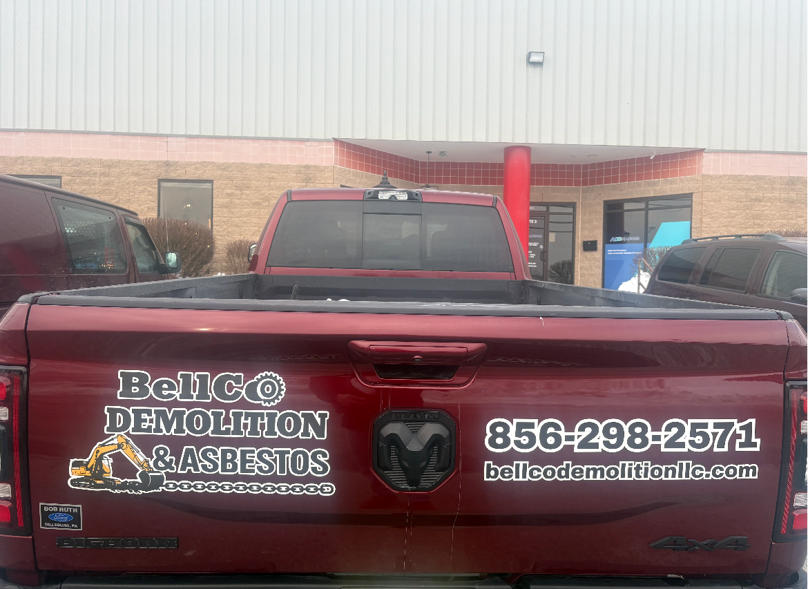 Red truck tailgate with “Rolico Demolition Services” and phone number at a worksite entrance