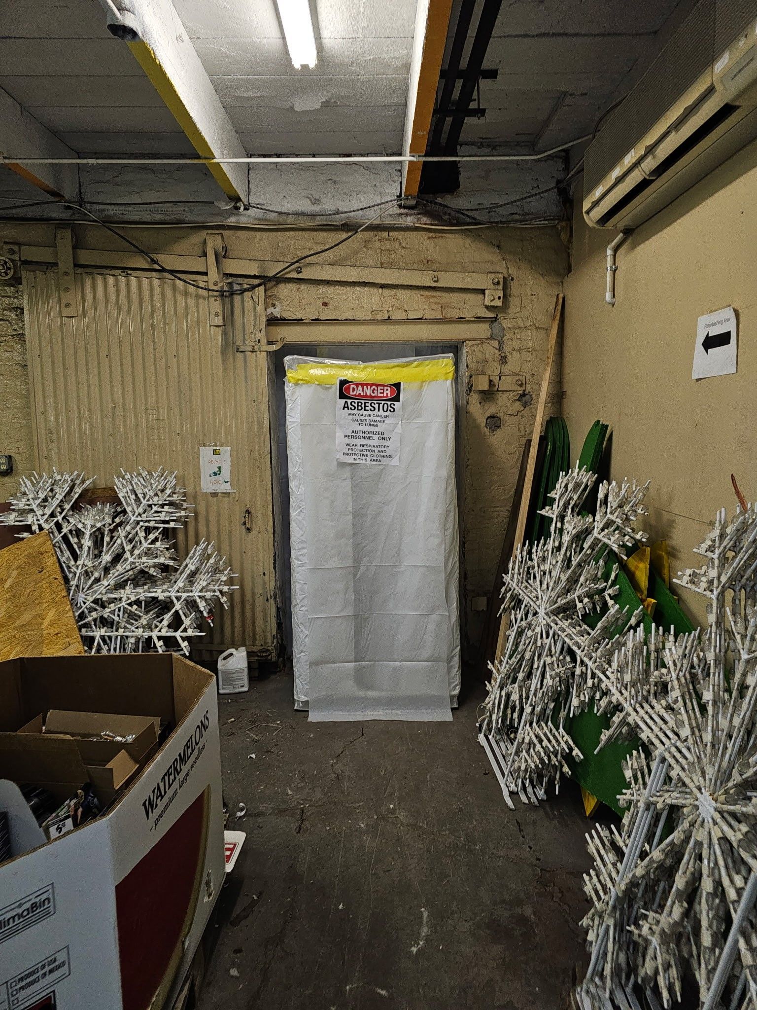 Narrow storage room with stacked white metal racks, a white door at center, and boxes on the left.