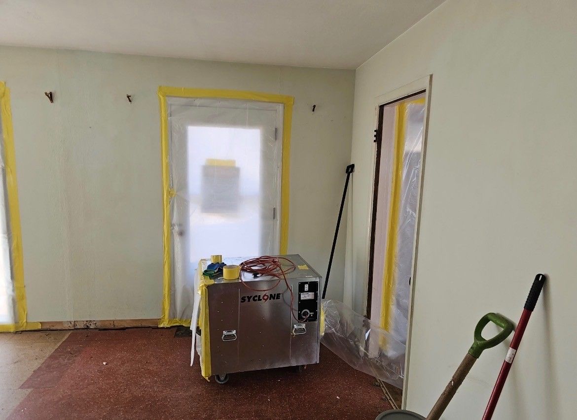 Unfinished room with taped windows, white walls, red floor, and a work cart in the center.