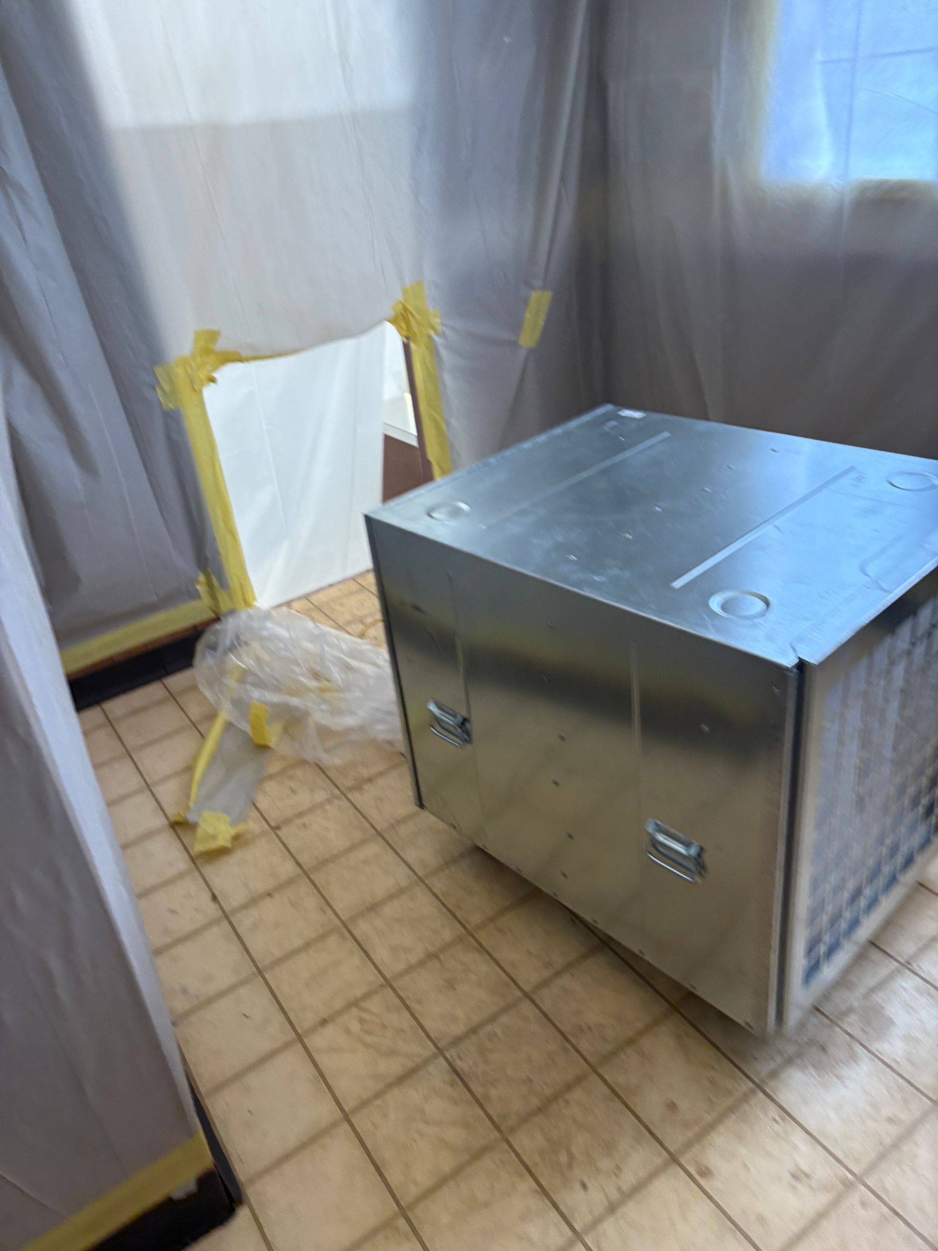 Metal utility cabinet on tiled floor beside a taped-off doorway in a curtained room