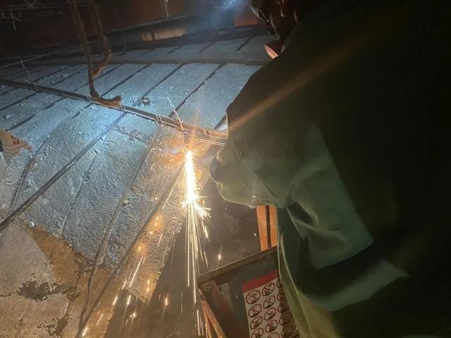 Worker cutting metal with sparks flying at night on a rooftop