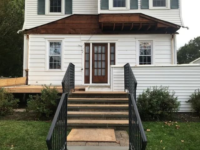 Front steps and wheelchair ramp leading to a white house entrance with a brown awning and black railings