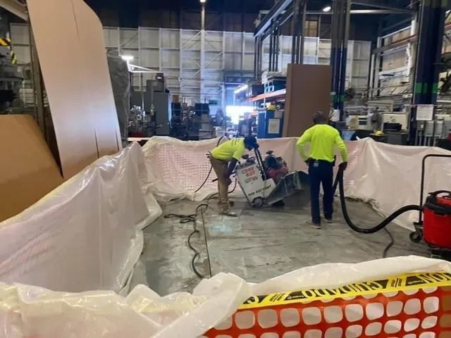 Workers in neon shirts operating equipment in a warehouse aisle, with plastic sheeting and barriers around the area