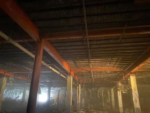 Dim unfinished interior with steel beams, exposed ceiling, and orange-lit columns in a large construction space