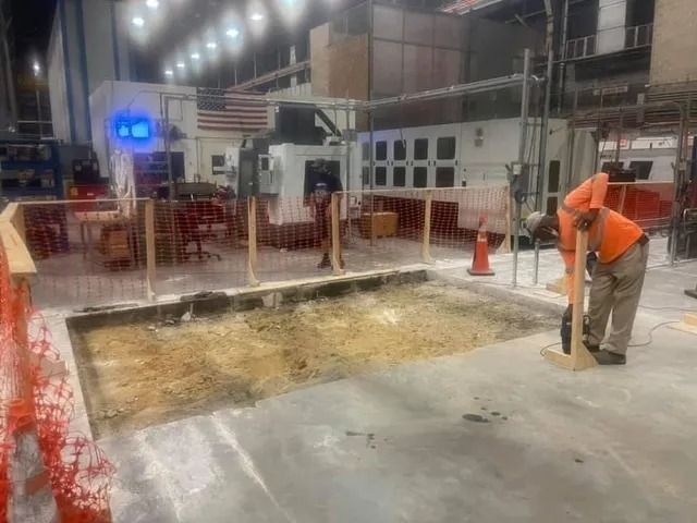 Indoor construction site with a worker measuring a large floor cutout using a long tool.