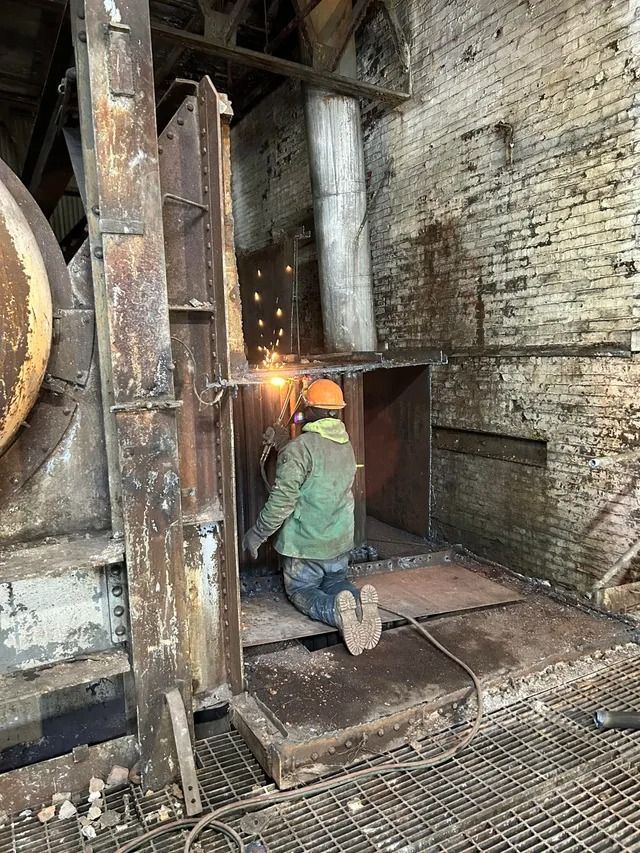 Worker welding inside an industrial furnace, sparks flying in a brick-lined facility