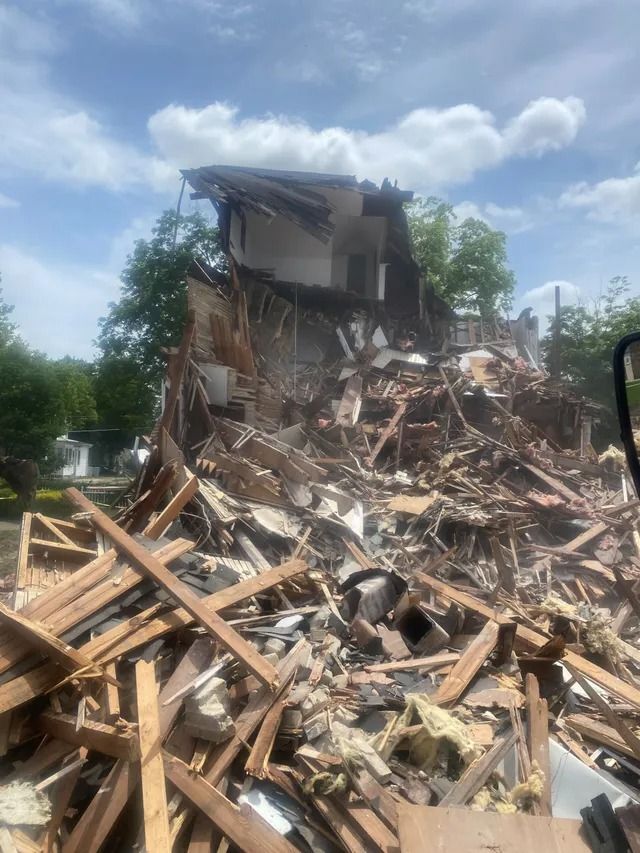 Collapsed house with a large pile of debris and broken wood under a cloudy sky