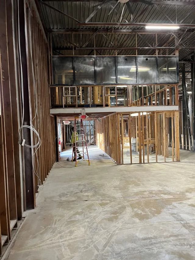 Interior construction site with exposed framing, concrete floor, and unfinished walls and ceiling