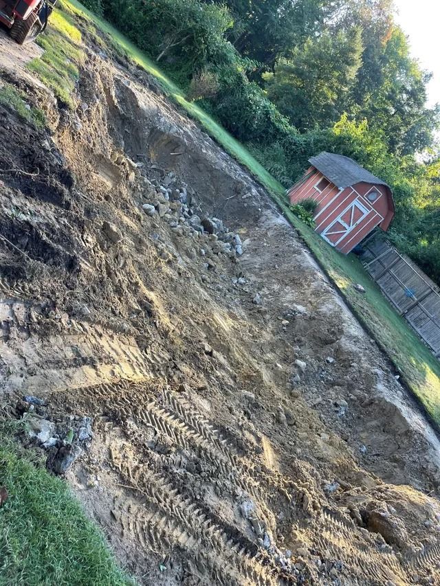 Tilted view of a muddy, freshly graded yard with a red shed and wooden fence in the background