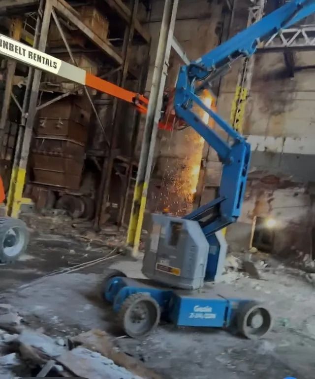 Blue Genie boom lift in a damaged warehouse interior with debris and metal beams
