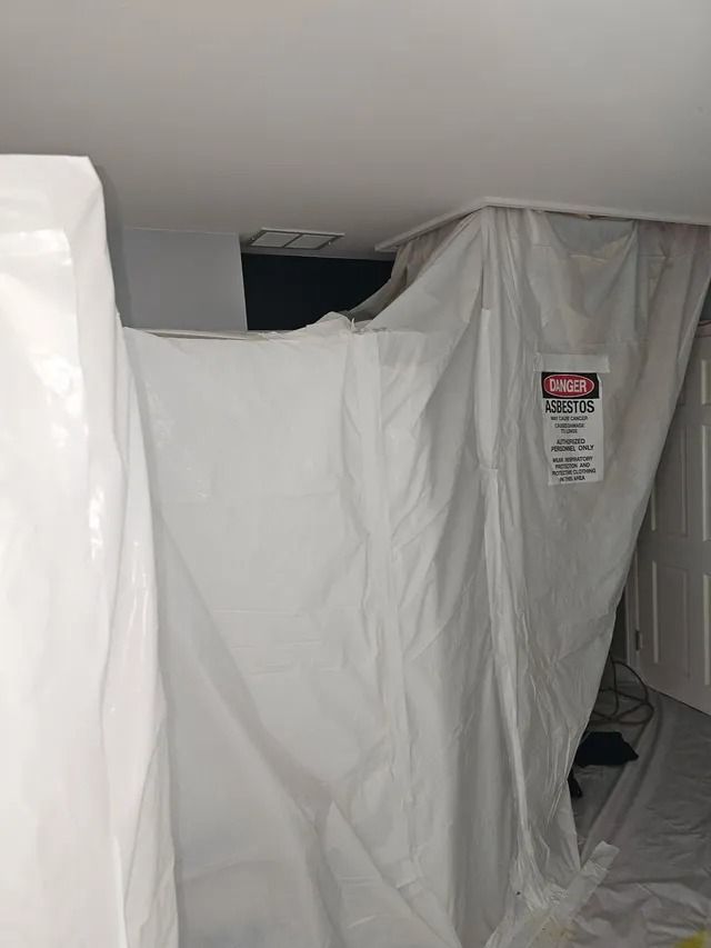 White plastic sheeting hung as a makeshift barrier in a narrow indoor space, with a warning sign on it.