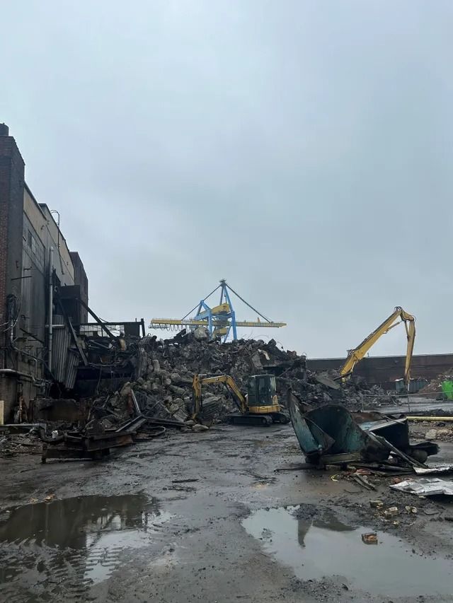 Flood-damaged industrial site with debris, puddles, and excavators under a gray sky