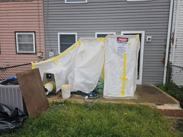 Plastic-covered structure with yellow tape against a house, with yard items nearby