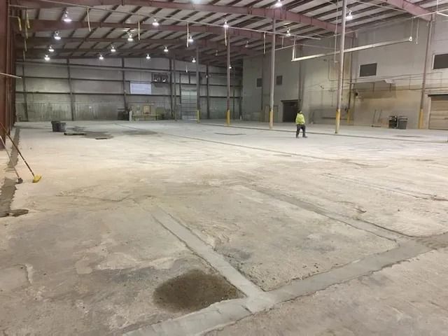 Empty warehouse interior with concrete floor and a person in a high-visibility vest near the back wall