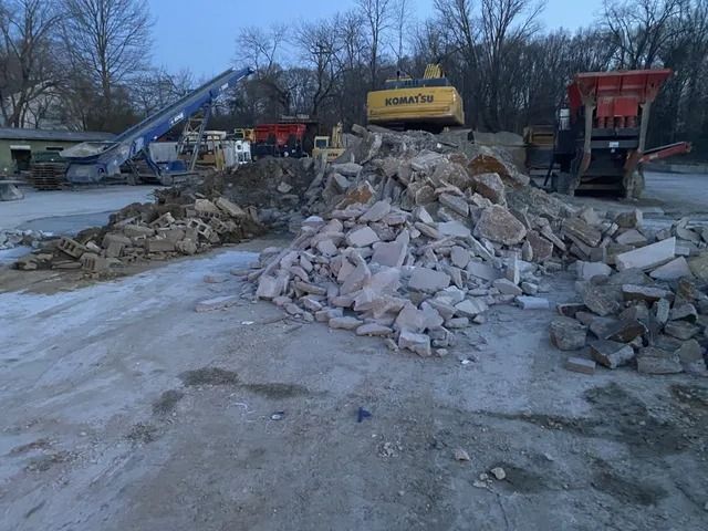 Road construction site with an excavator and dump trucks behind piles of broken concrete rubble