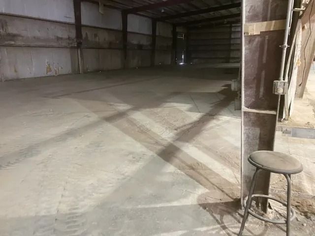 Empty warehouse interior with concrete floor, metal walls, and a stool near the right side.