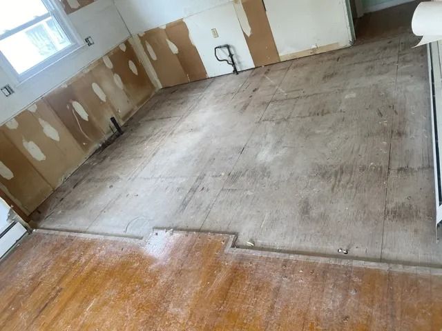 Empty room with unfinished drywall, bare concrete floor, and wood flooring in foreground