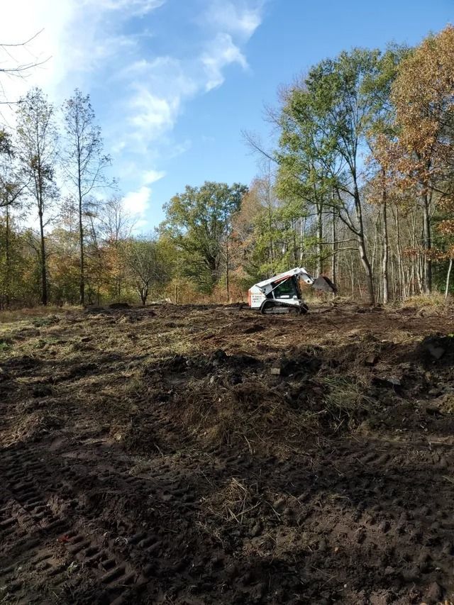 White excavator clearing brush in a wooded field under a blue sky