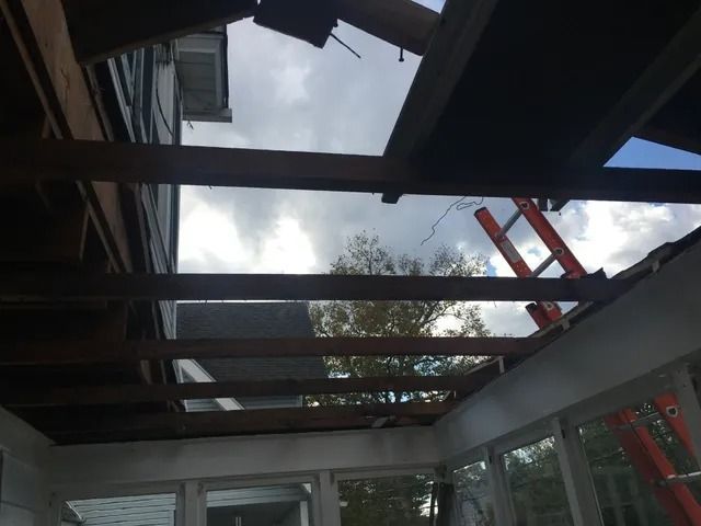 Damaged roof with exposed beams and skylights, viewed from inside a building during repairs