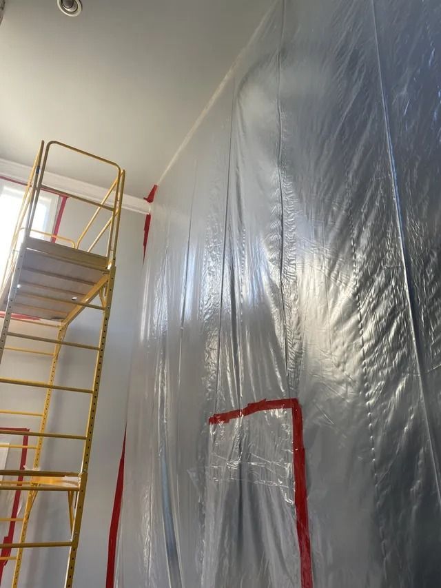 Plastic-covered wall with red tape, next to a yellow scaffold in a hallway under renovation