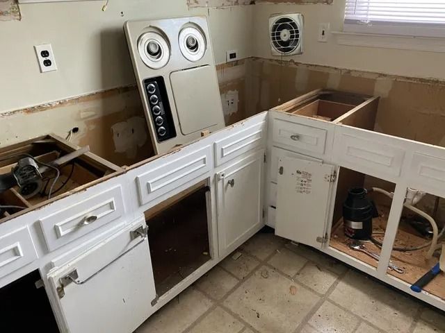 Kitchen under renovation with white cabinets, exposed countertops, and a dishwasher or appliance on the floor.