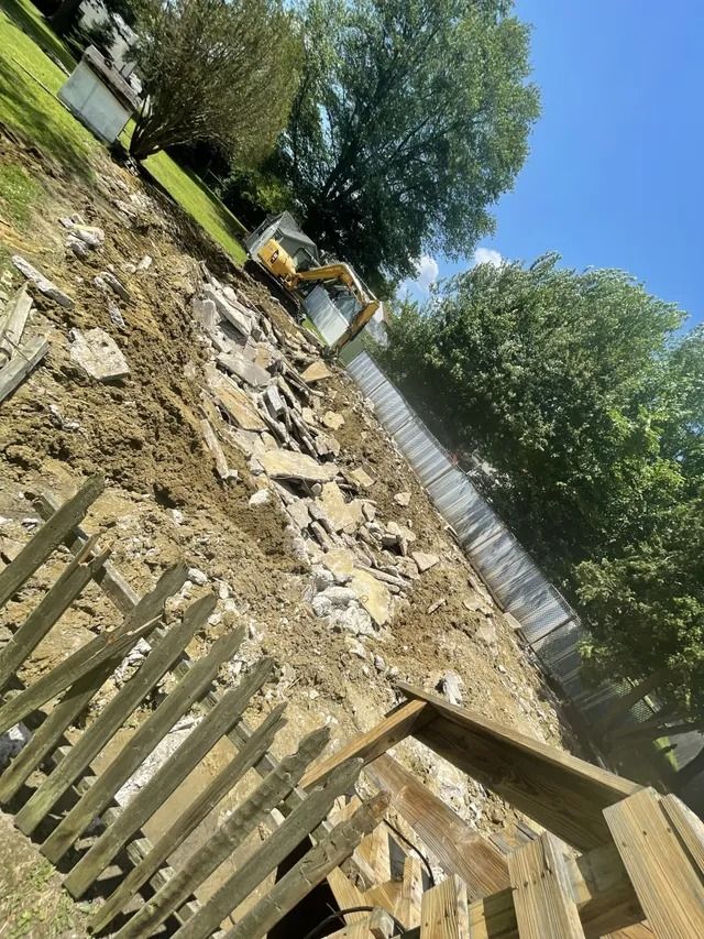 Backyard garden with scattered rocks, a white fence, trees, and a wooden gate in the foreground