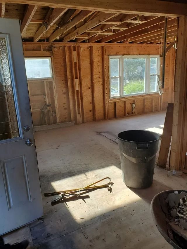 Partially finished room with exposed studs, window, open door, and construction bucket on the floor