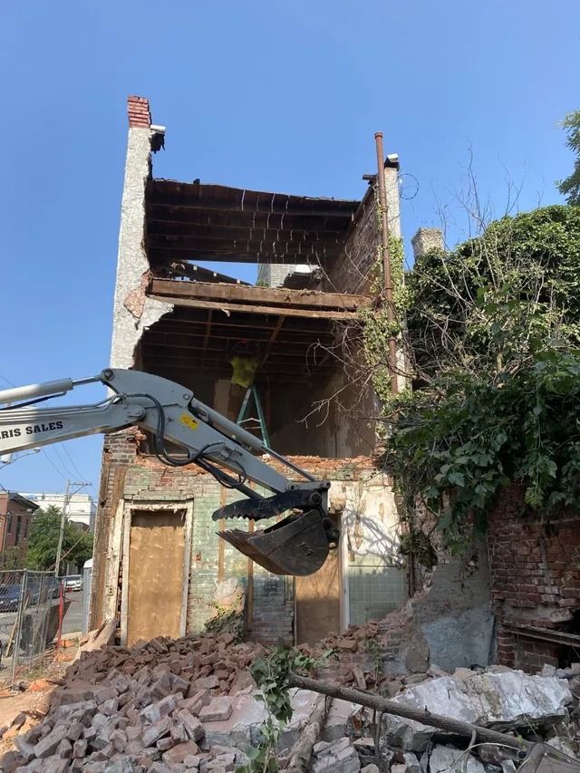 Demolition excavator tearing down a ruined two-story building with rubble in front
