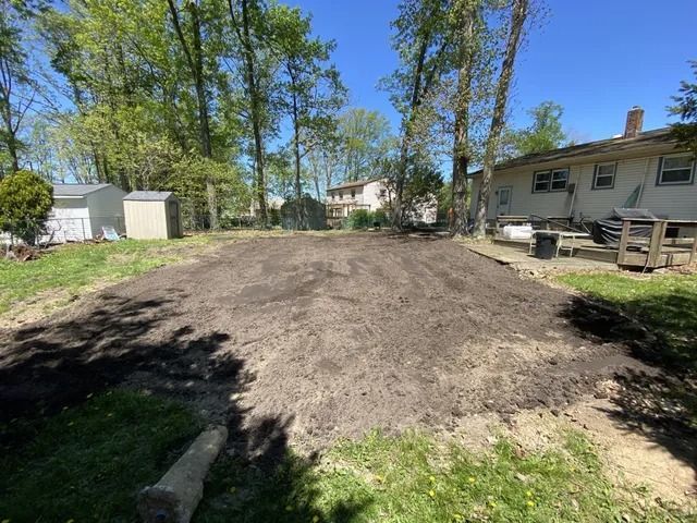Fresh dirt mound in a residential backyard beside a house and trees on a sunny day