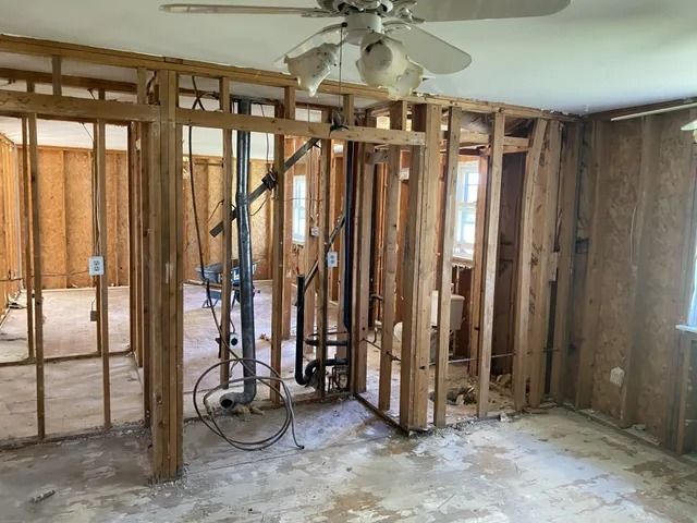 Damaged room interior with exposed wall studs, debris on floor, and a ceiling fan overhead