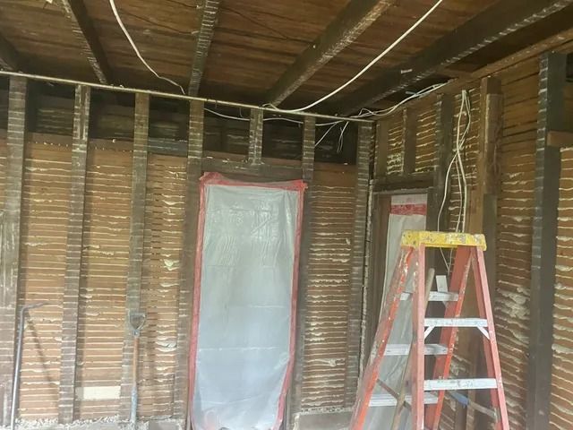 Interior of unfinished room with exposed insulation, covered windows, and a red ladder on the right.