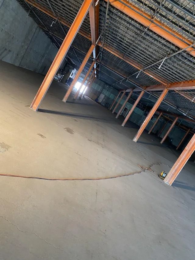 Tilted view of an empty industrial warehouse floor with orange metal beams and fencing overhead
