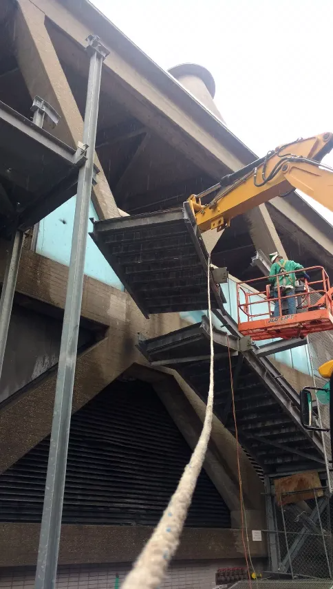 Workers in a lift repair a damaged roof edge on a building beside a large cable