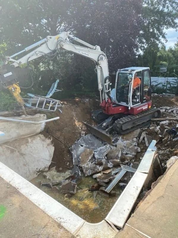 Excavator clearing rubble at a collapsed concrete structure beside muddy water